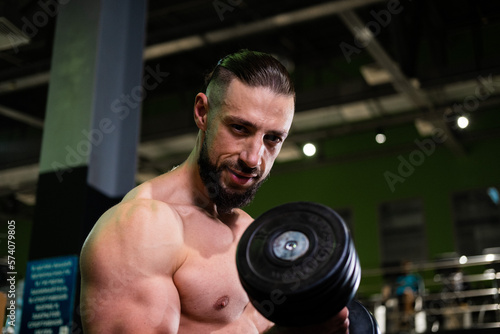 A handsome muscular male bodybuilder with a beard does a biceps exercise with a dumbbell