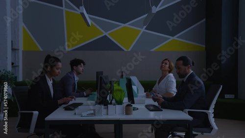 Workers, men and women in modern office working at computers, focused on work, turned off light, annoyed, tired, waiting for electricity to be turned on.