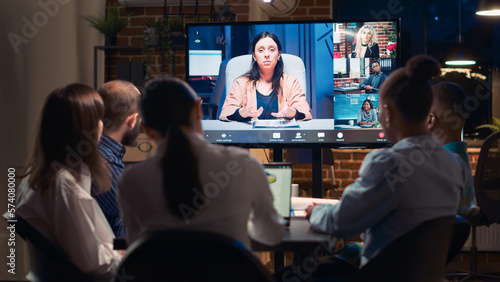 Employees listening to remote coworker in videocall conference, colleagues talking in videoconference at night time. Office workers chatting in teleconference in boardroom