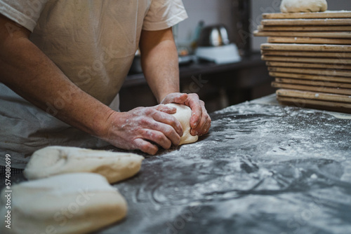 Fototapeta Naklejka Na Ścianę i Meble -  Baker kneading bread dough on messy counter full of flour in bakery