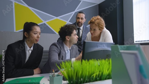 Employees, colleagues in the office gathered at the computer, discuss the document, solve work issues.