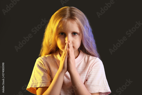 Little girl with lights in colors of Ukrainian flag praying on black background