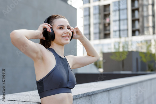 Happy sportswoman in headphones, getting ready for jogging through city streets. © Tymoshchuk
