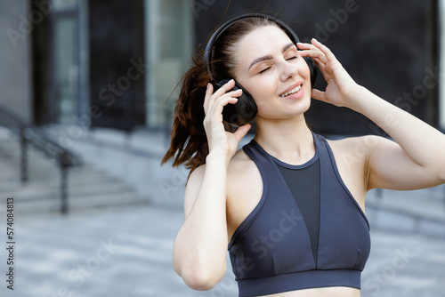 Excited young woman in sportswear listening music, while exercising outdoors.