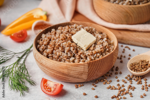 Wooden bowl of tasty buckwheat porridge with butter on grey table