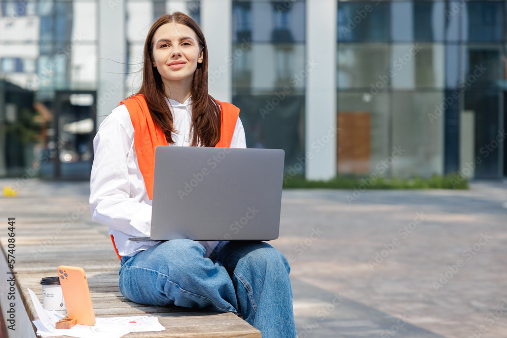 Cheerful brunette woman working on laptop, while sitting on bench. Cheerful brunette woman working on laptop, while sitting on bench.
