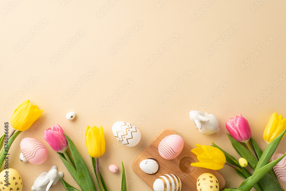 Easter celebration concept. Top view photo of colorful easter eggs in wooden egg holder ceramic rabbits yellow and pink tulips on isolated pastel beige background with copyspace