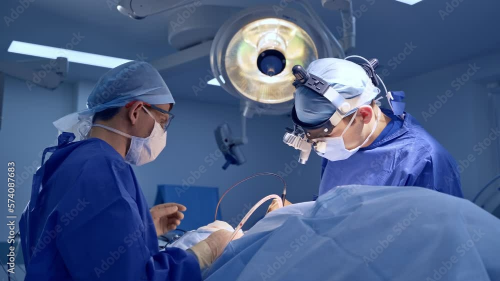 Caucasian male neurosurgeon electric instrument in surgery. Assistant watching the operation carefully ready to help. Caucasian male neurosurgeon electric instrument in surgery. Assistant watching the operation carefully ready to help.