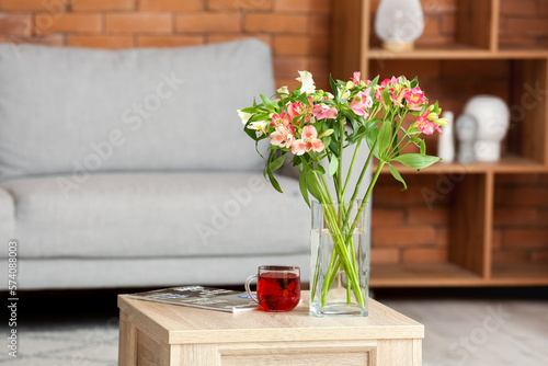 Vase with alstroemeria flowers, cup of tea and magazine on table in living room photo