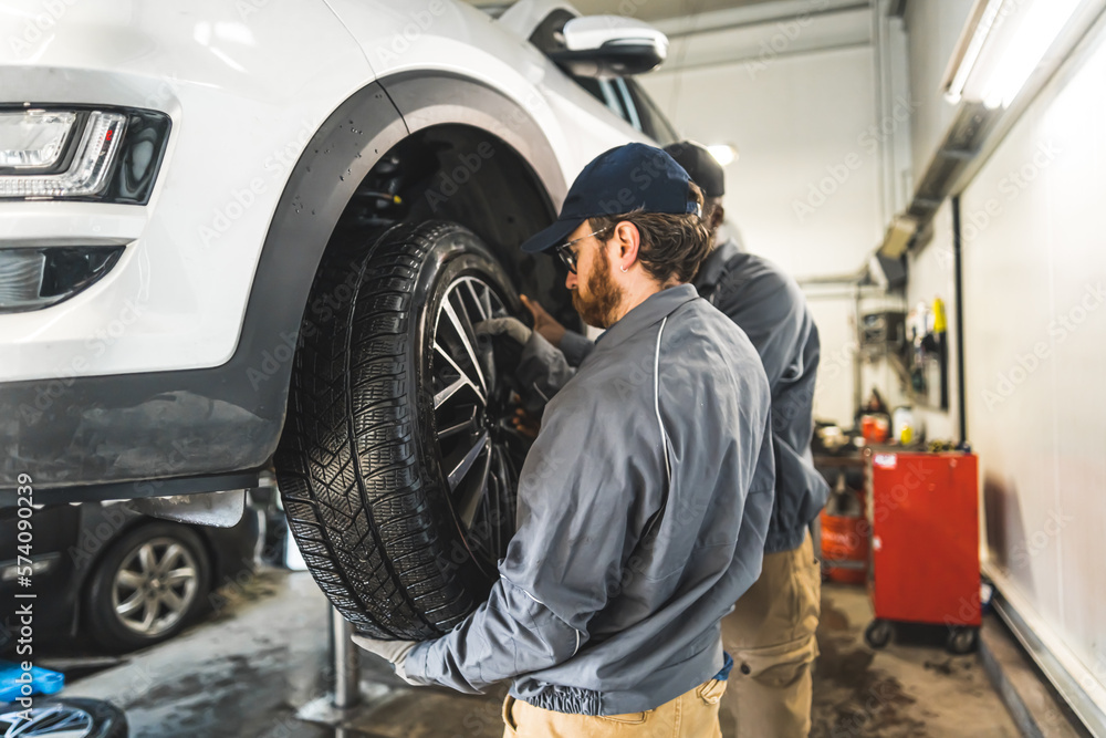 Medium shot of one mechanic replacing a car tyre and other one helping him. High quality photo