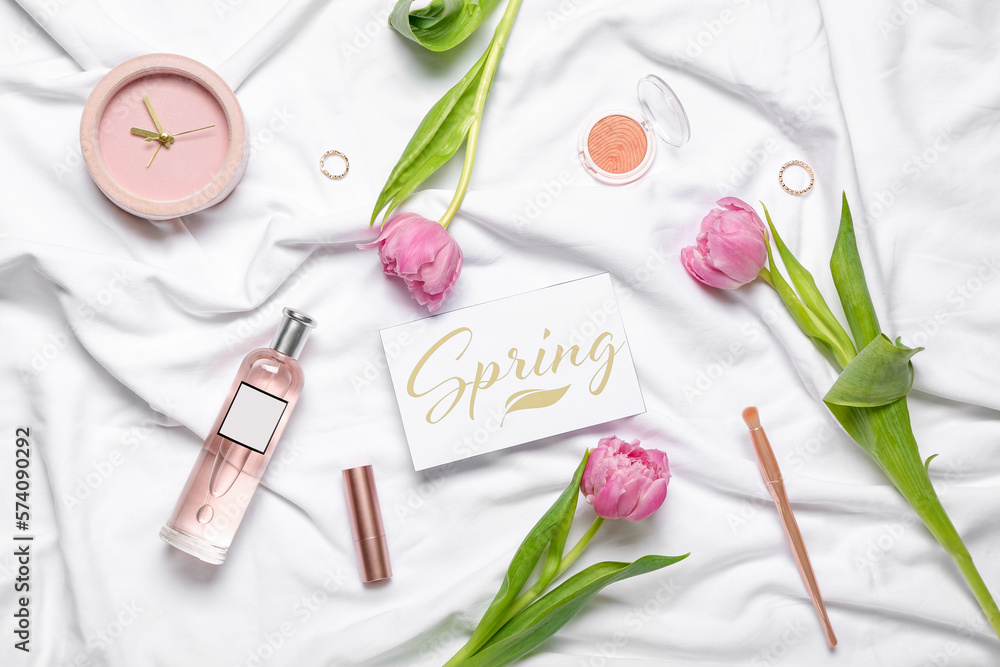 Composition with cosmetics, tulip flowers, alarm clock and card on light fabric background Composition with cosmetics, tulip flowers, alarm clock and card on light fabric background