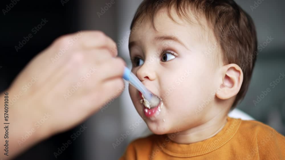 Face of a cute Caucasian toddler eating well from spoon. Close up. Mom is feeding her son from spoon. Face of a cute Caucasian toddler eating well from spoon. Close up. Mom is feeding her son from spoon.