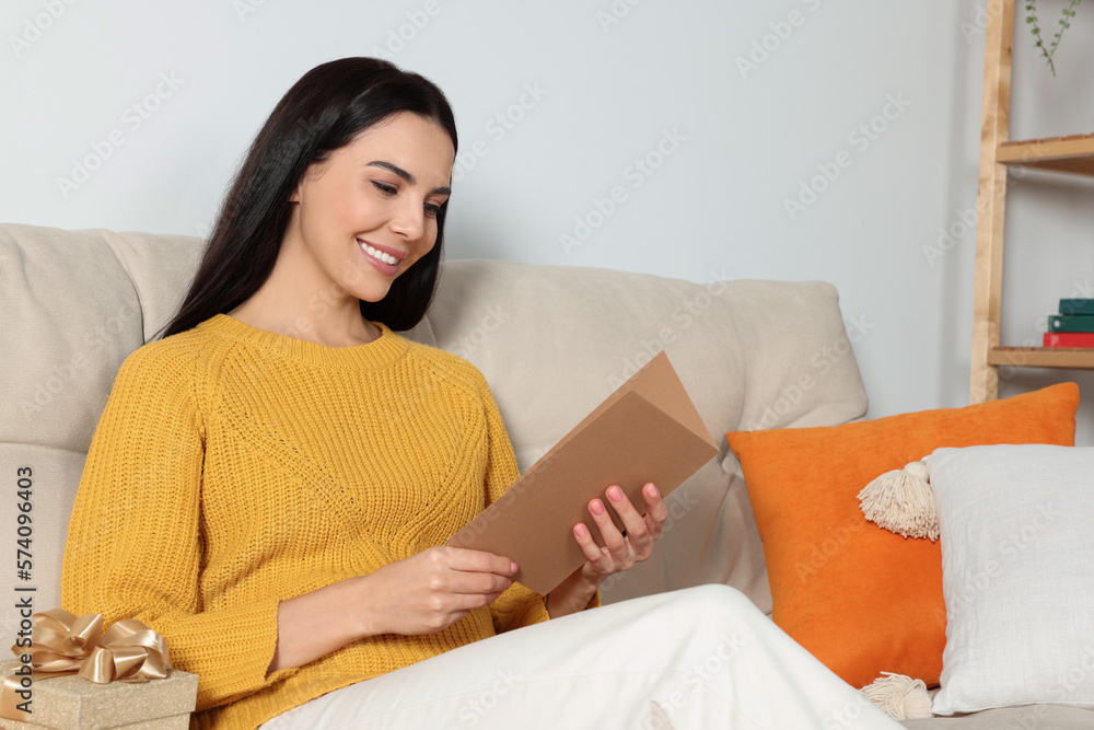 Happy woman reading greeting card on sofa in living room Happy woman reading greeting card on sofa in living room
