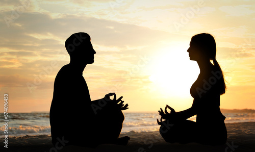 Silhouette of lovely couple meditating together on beach at sunset