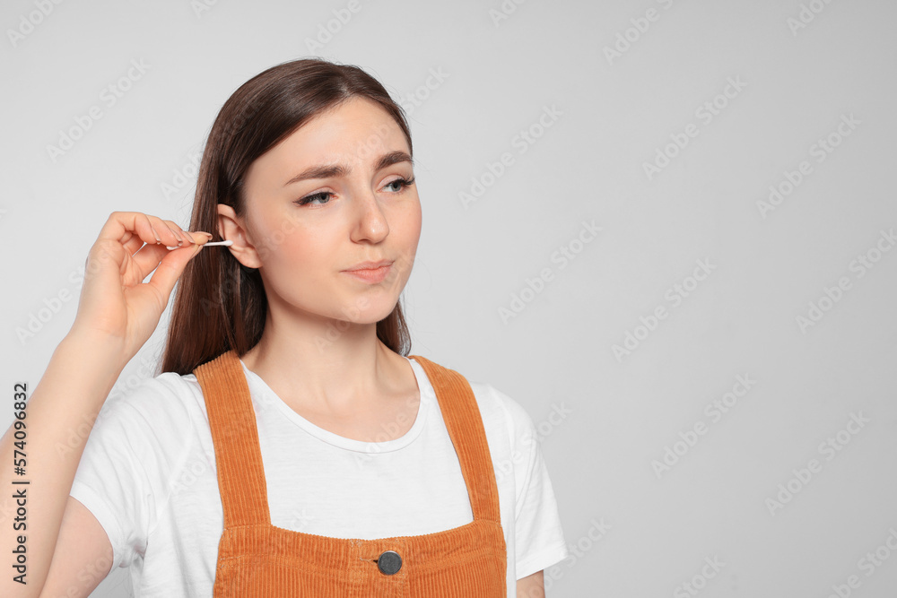 Young woman cleaning ear with cotton swab on light grey background. Space for text Young woman cleaning ear with cotton swab on light grey background. Space for text