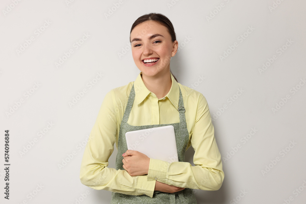 Beautiful young woman in clean apron with tablet on light grey background Beautiful young woman in clean apron with tablet on light grey background
