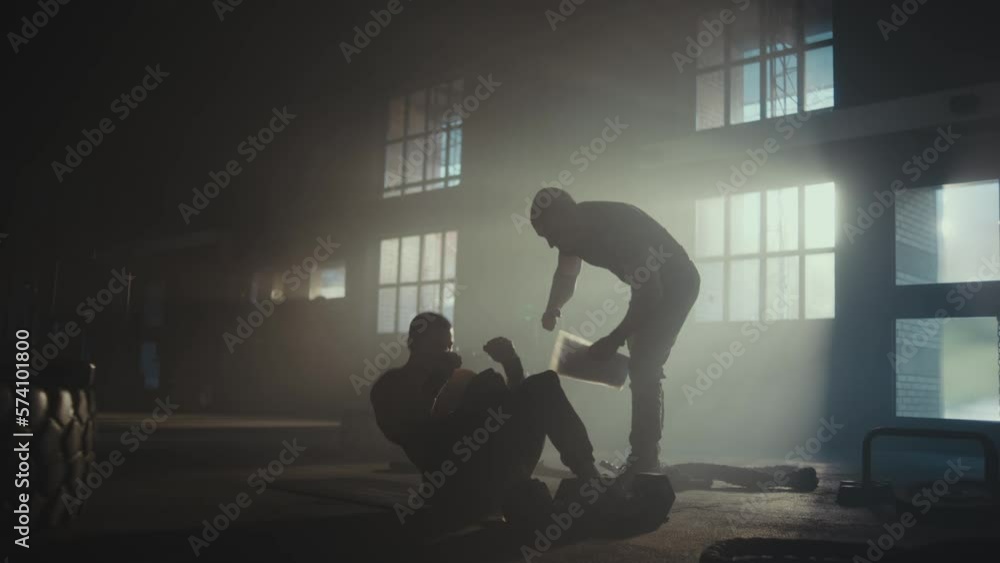 Slow-motion shot of a man with personal trainer doing sit ups at the gym. Fitness, sport, training and healthy lifestyle concept Slow-motion shot of a man with personal trainer doing sit ups at the gym. Fitness, sport, training and healthy lifestyle concept