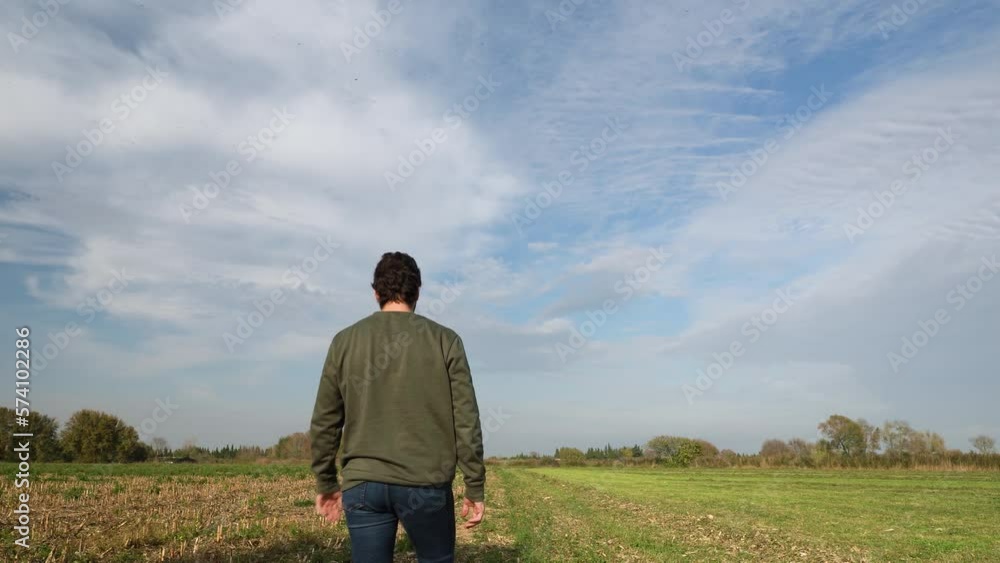 A young man walking into a field in a sunny day. Male model with a green sweater walking through a flat field in the center of the shot, Realizing that he has forgotten something, he turns to go back. A young man walking into a field in a sunny day. Male model with a green sweater walking through a flat field in the center of the shot, Realizing that he has forgotten something, he turns to go back.