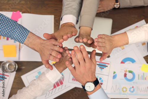 Office employees joining hands at work, top view