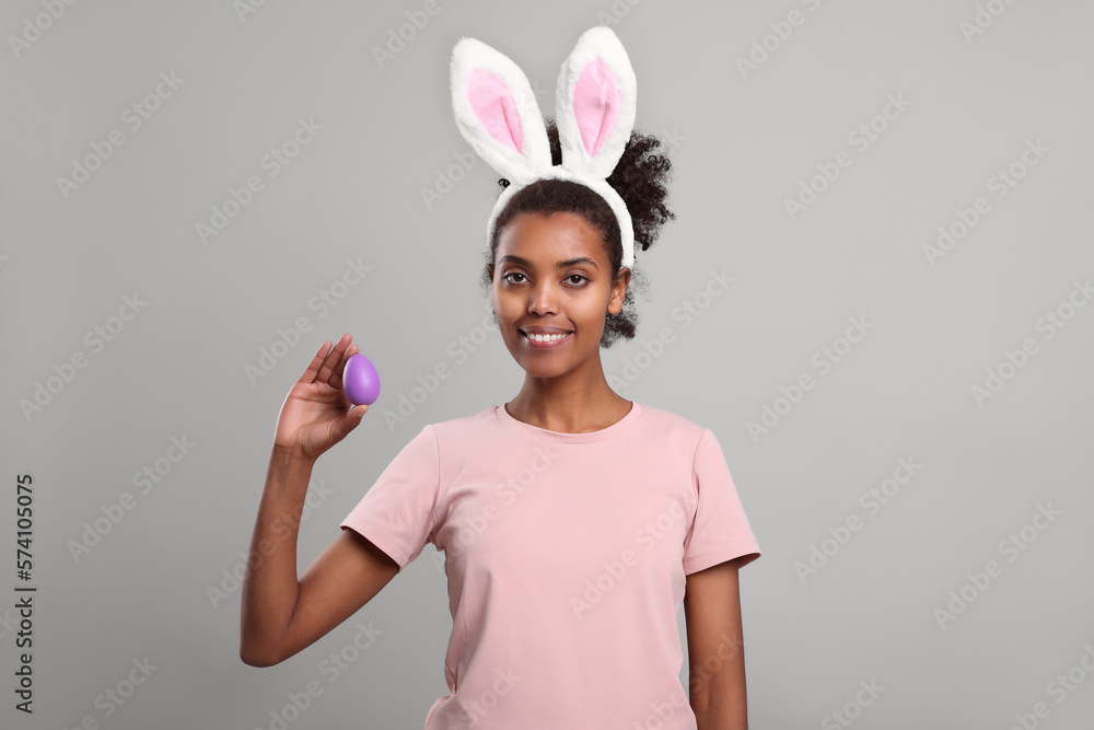 Happy African American woman in bunny ears headband with Easter egg on gray background Happy African American woman in bunny ears headband with Easter egg on gray background