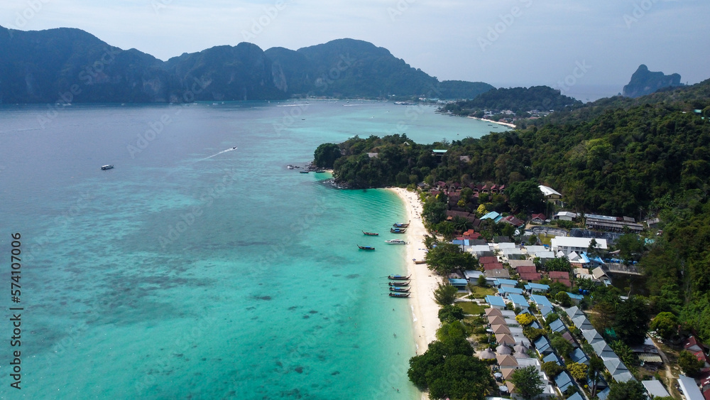 Aerial view of beautiful white sand beach and turquoise waters of Andaman Sea, Phi Phi, Krabi, Thailand. Traditional longtail boats and Tonsai bay at distance. 