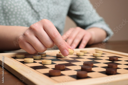 Playing checkers. Woman thinking about next move at wooden table, closeup