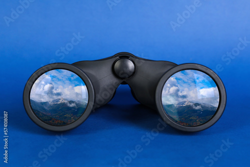 Fototapeta Naklejka Na Ścianę i Meble -  Binoculars on blue background. Mountain landscape reflecting in lenses