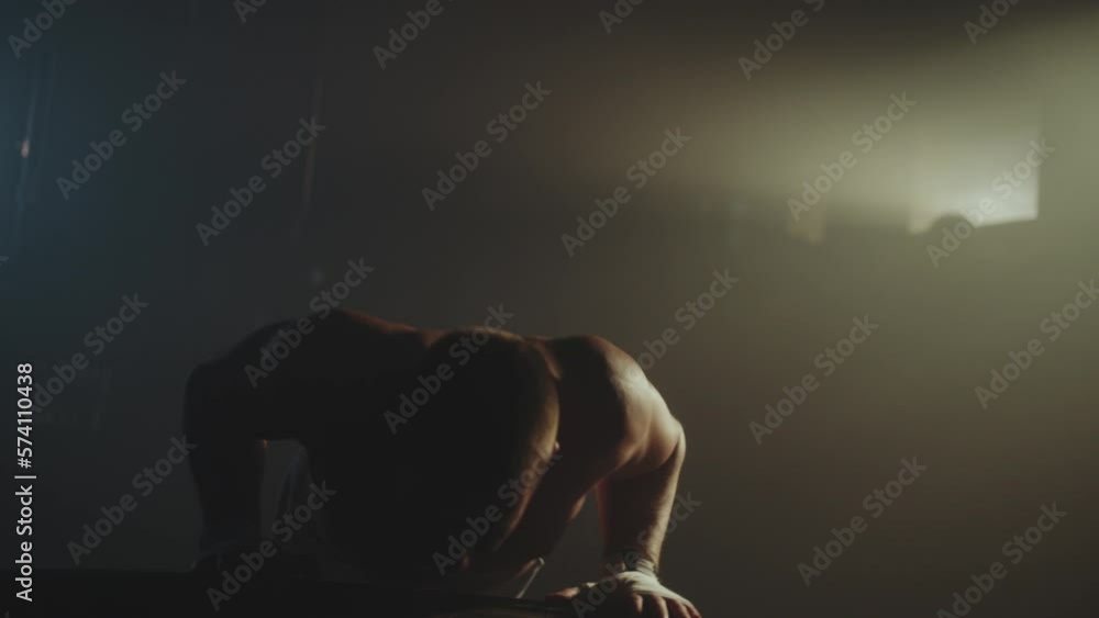 Athletic young man performing push ups on tyre, exercising at warehouse enjoying physical activity