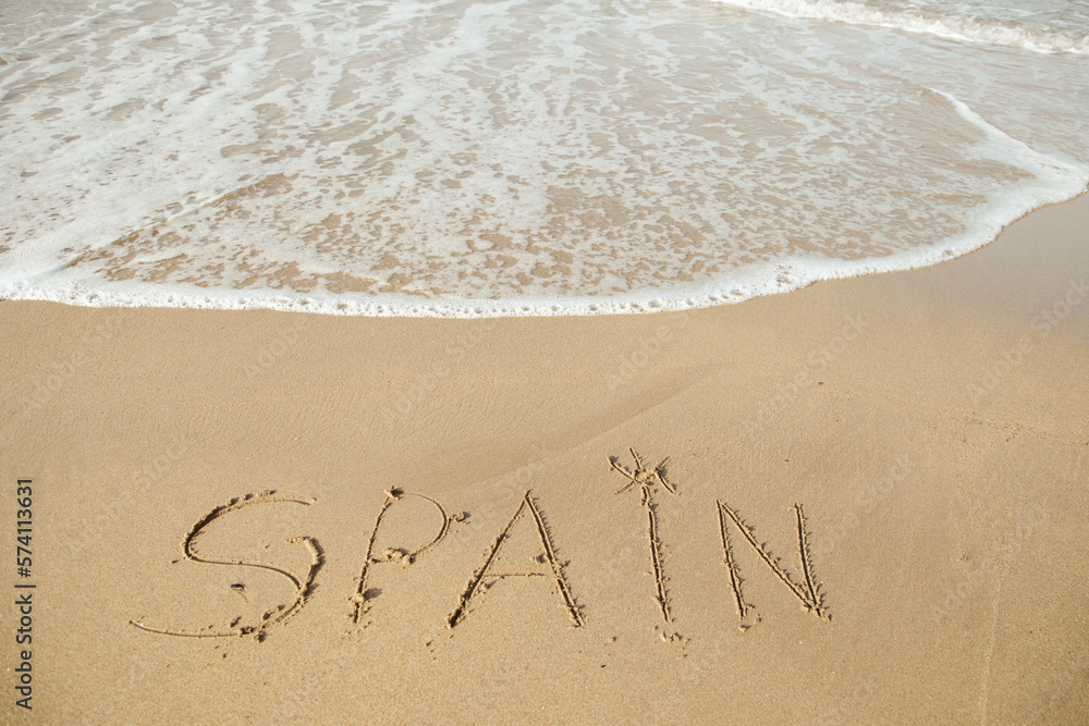 Spain lettering on the beach with wave and clear blue sea. 