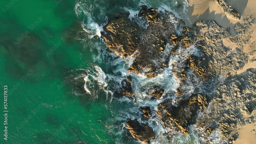 Aerial view of Waves crashing onto rocks. Top view of fabulous sea tide on a sunny day. Drone filming breaking surf with foam in sea of cortez on east cape near san jose del cabo Aerial view of Waves crashing onto rocks. Top view of fabulous sea tide on a sunny day. Drone filming breaking surf with foam in sea of cortez on east cape near san jose del cabo
