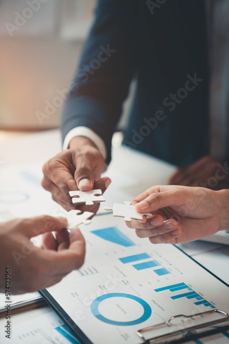 A group of Asian businessmen holding a jigsaw together are meeting the office. They are meeting on finance and managing business policies perfectly according to the model and laid out the plan.