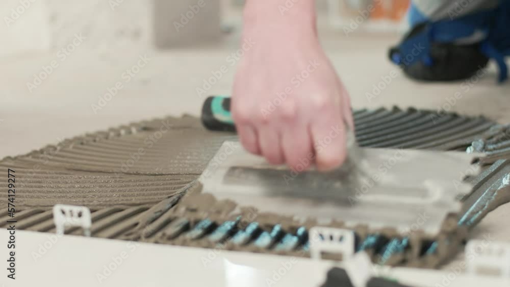 Construction worker spreading tile adhesive on the cement floor for placing tiles. Contractor tiler installing tiles. Construction worker spreading tile adhesive on the cement floor for placing tiles. Contractor tiler installing tiles.