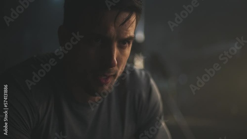 Close-up shot of a tired young man breathing heavily after doing kettelbell lifting exercise while group of people exercising in blurry background