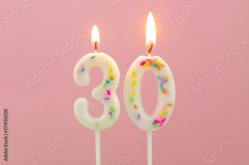 White decorated burning birthday candles on pink background, number 30 photo