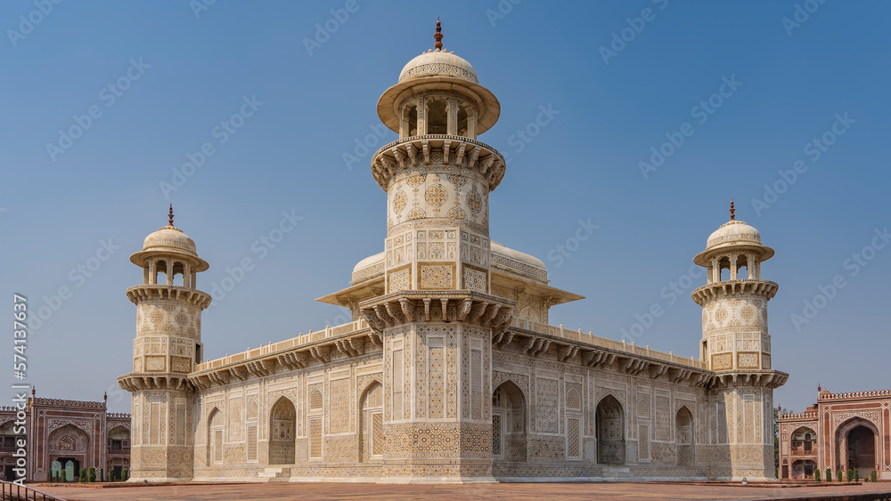 Beautiful symmetrical marble tomb of Itmad-Ud-Daulah on a blue sky background.   Mausoleum with minarets, domes, arches. The walls are decorated with ornaments, inlays of precious stones. India. Agra.