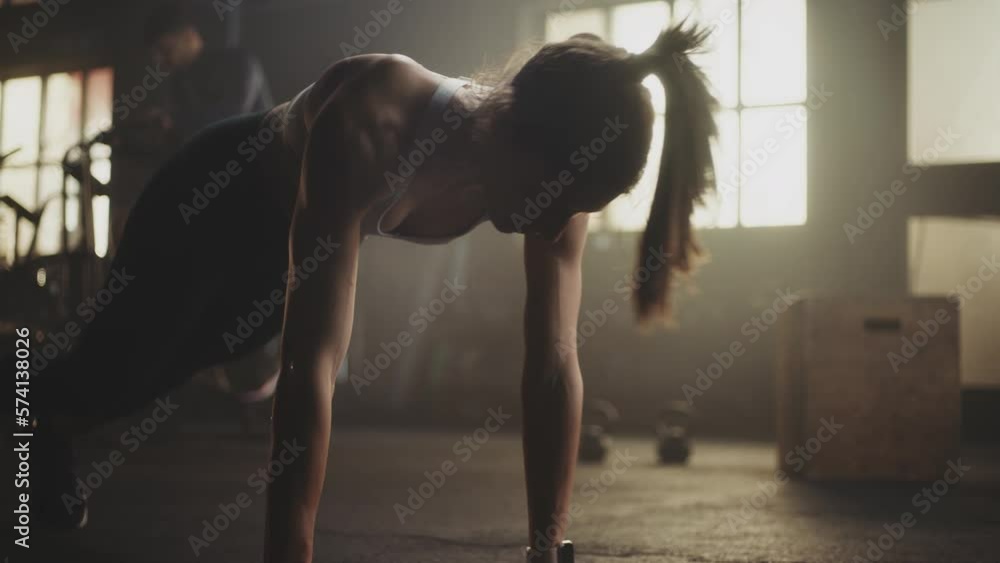 Slow-motion shot of a fit caucasian woman doing push-up exercise on the floor at gym. Two men working out in the background.