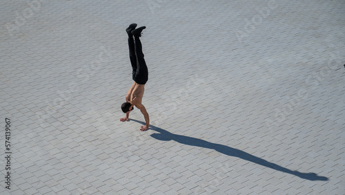 Shirtless man walks on his hands outdoors. View from above.