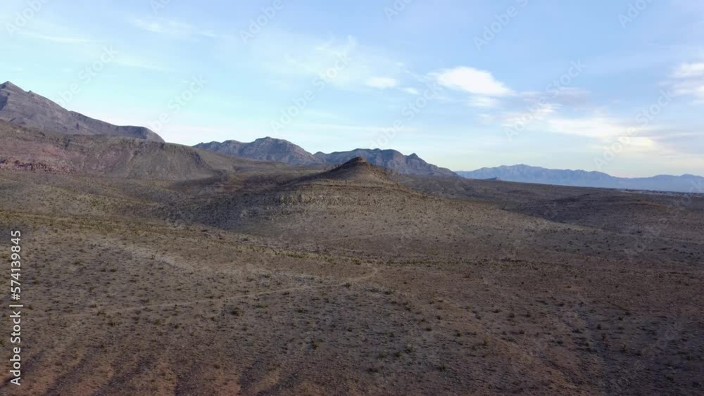 Aerial shot of a single, lone hill peaking through the desert landscape with stunning mountains in the background. This drone clip was filmed at sunrise near Red Rock in Las Vegas, Nevada. Aerial shot of a single, lone hill peaking through the desert landscape with stunning mountains in the background. This drone clip was filmed at sunrise near Red Rock in Las Vegas, Nevada.