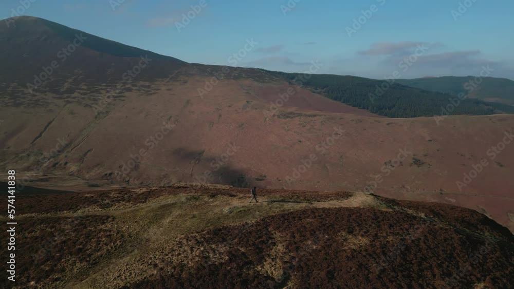 Hiker walking on hillside in winter with slow reveal of valley and lake beyond in English Lake District UK Hiker walking on hillside in winter with slow reveal of valley and lake beyond in English Lake District UK