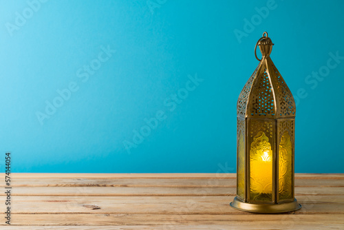 Lightened lantern on wooden table over blue background. Ramadan kareem holiday celebration concept