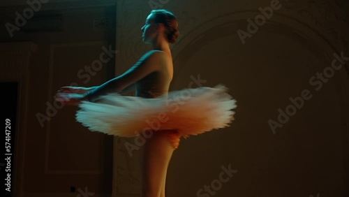 Cinematic shot of elegant ballerina in ballet dress performing on dim theater stage. Female ballet dancer on choreography rehearsal in opera, practices spinning movement. Classical theatrical ballet.