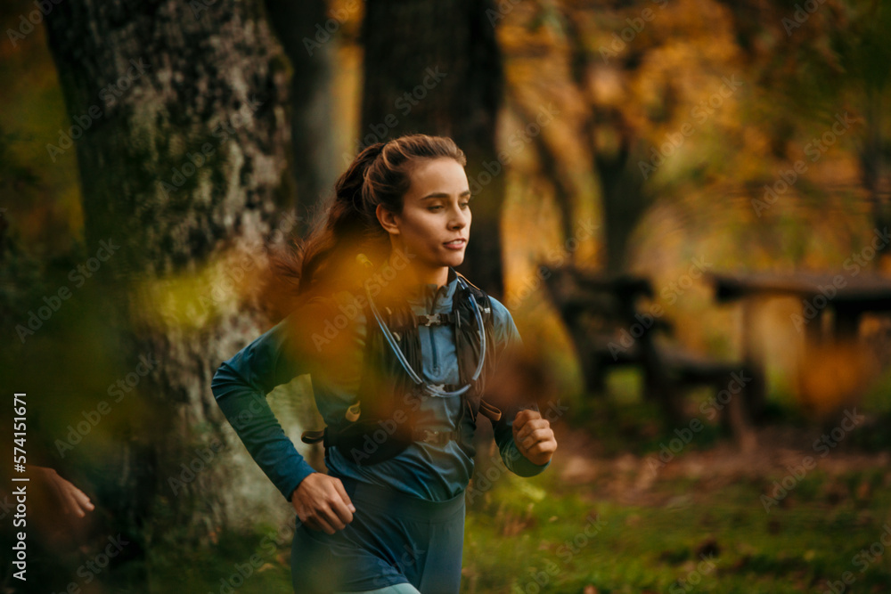 A young female jogger running in the forest. A woman is wearing a running vest during a cross-country race