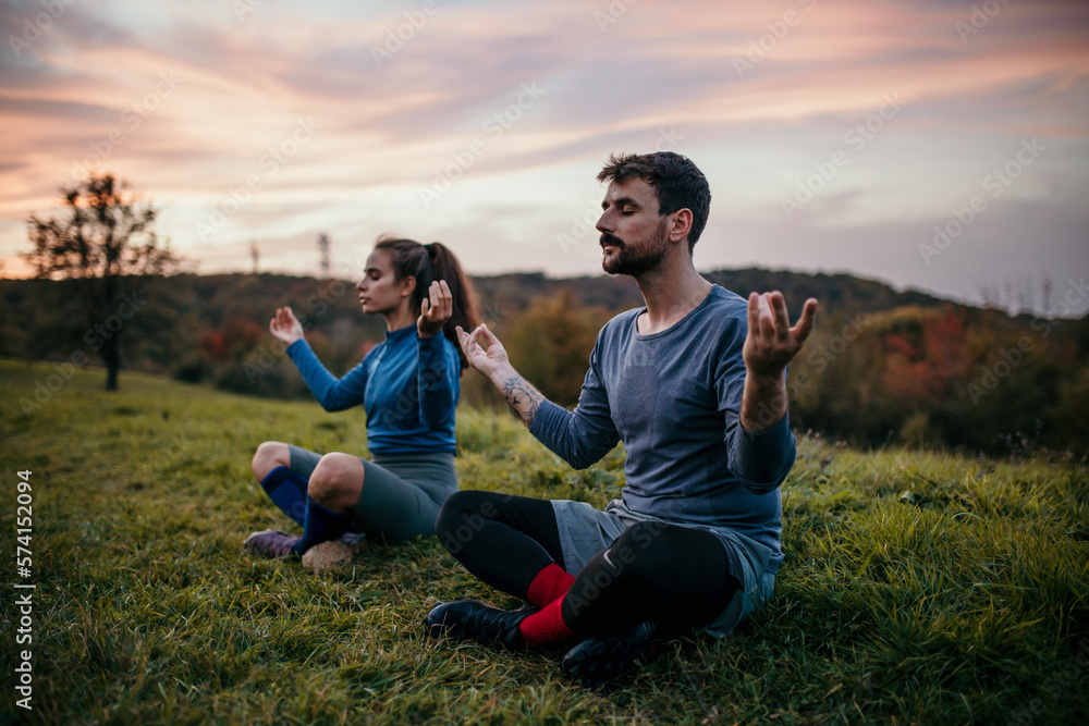 Two people, a couple, sitting and practicing yoga in sports clothing after a jog. Two people, a couple, sitting and practicing yoga in sports clothing after a jog.