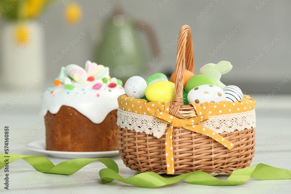 Easter basket with painted eggs near tasty cake on white marble table