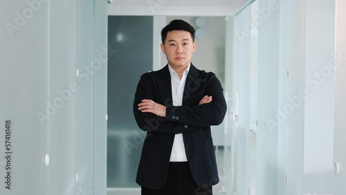 Focused confident young asian man, male chinese face looking at camera crossing hands in office, professional succsessful freelancer posing in office hallway, close up front business portrait. photo