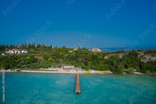 Wooden pier, turquoise water. Panoramic aerial view of Lido delle Bionde beach, Sirmione, Lake Garda, Italy.