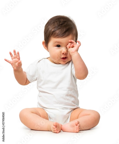 Cute baby rubbing eyes in white onesie on white background
