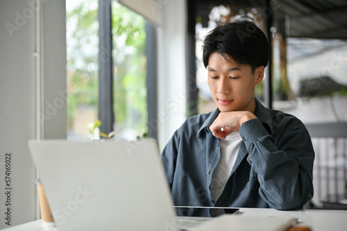 Focused Asian man looking at tablet screen  pensively thinking about his marketing project
