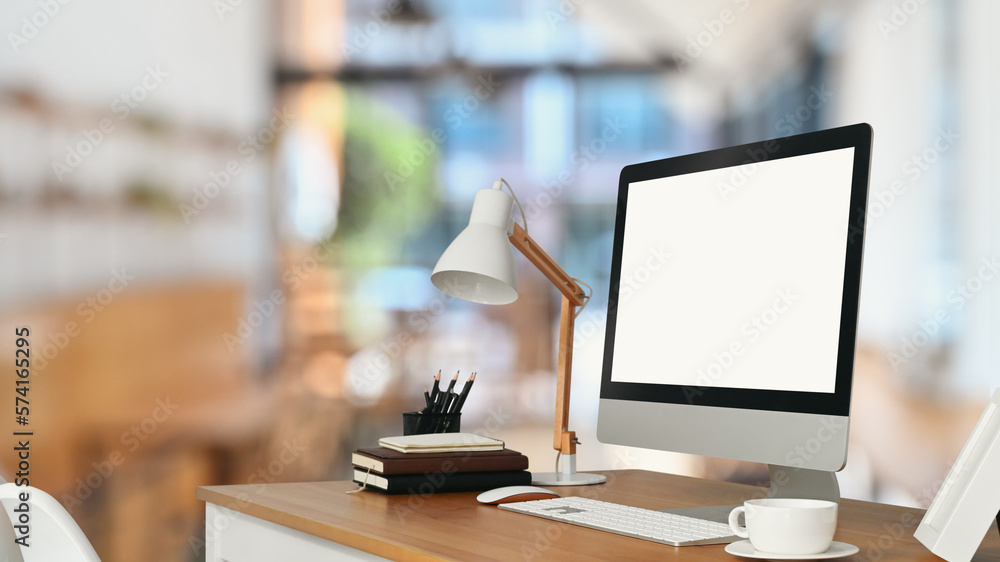Bank screen computer monitor, lamp, coffee cup and books on wooden table against blurred home office interior background Bank screen computer monitor, lamp, coffee cup and books on wooden table against blurred home office interior background