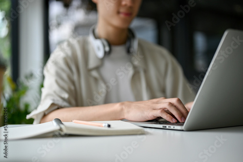 Focused Asian male college student typing on keyboard, browsing internet, using laptop